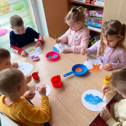 Dzieci z przedszkola Sezamkowe podczas zajęć plastycznych, malowanie farbami przy wspólnym stole.